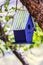 Purple bird nest hanging from tree with tin roof reflecting leaves - all but bird house blurred - closeup