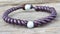 a purple bracelet with two white beads on a wooden surface with a black bead clasp and a brown leather cord with a white bea