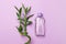 Purple cosmetic bottle with bamboo stalk on purple background