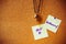 Purple handwriting on white paper note, pin on cork board with yellow and purple pin, metal skull pendant necklace as background