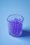 Purple marbles in drinking transparent glass blue background angle view
