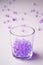 Purple marbles in drinking transparent glass with scattered marbles on white background