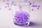 Purple marbles in drinking transparent glass with scattered marbles on white background