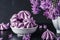 Purple meringue cookies with lilac flowers in vase on dark background. low key. still life