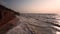 Purple and pink sunset view on the beach with sandy clay breakage and slow shutter speed sea waves and rocks seascape