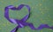 Purple ribbon heart with golden confetti on green background. Mardi gras greeting card