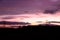 A purple sky sunset over a silhouetted countryside with power pylons