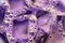 Purple soapy liquid with bubbles closeup, cloudy water texture with transparent ice cubes and bubbles