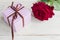 Purple striped gift box with brown ribbon bow and bautiful red rose on wooden background. Greeting card for holiday