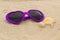 Purple sunglasses shaped heart with shells on the sand