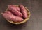 Purple yams pile on a basket on a dark brown background.