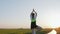 A purposeful woman stands on one leg and performs yoga exercises. The girl is engaged in sports at sunset