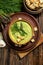 Purred creamy asparagus soup in glass bowl on black plate against raw fresh asparagus and greenery