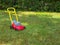 Push lawn mower toy on the grass in a garden . No people