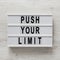 `Push your limit` words on a lightbox on a white wooden surface, top view. Overhead, from above, flat lay. Close-up