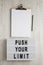 `Push your limit` words on a modern board, clipboard with blank sheet of paper on a white wooden background, top view. Overhead,