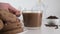 Putting glass coffee cup on white table with chocolate cookies. Close up.