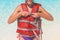 Putting on life jacket for water sport. Woman wearing personal flotation device vest on ocean