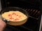 Putting a pan with homemade pizza with sausages, tomatoes and cheese in hot air oven close up with selective focus