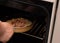 Putting a pan with homemade pizza with sausages, tomatoes and cheese in hot air oven by senior woman hand close up with