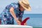 Putting a red fin into a surfboard, Japanese teen wearing an Hawaiian shirt and straw hat.