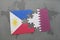 puzzle with the national flag of philippines and qatar on a world map background.