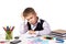 Puzzled bored pupil sitting at the desk with hand under the head surrounded with stationery