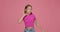 Puzzled child girl putting hands near ears to listen better, laughing at joke on pink background. Hearing problems
