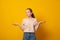 Puzzled girl, spreads hands with doubt,over yellow background. Teen girl faces dilemma