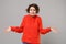 Puzzled perplexed young brunette woman girl in casual red hoodie posing isolated on grey wall background studio portrait