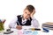 Puzzled sad writing pupil sitting at the desk surrounded with stationery looking straight at the camera