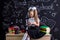 Puzzled schoolgirl sitting on the desk with books, school supplies, doing maths with calculator