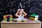 Puzzled schoolgirl sitting at the desk with books, school supplies, holding her both hands over the head