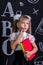 Puzzled schoolgirl standing before the chalkboard as a background with a couple of books holding them and pointing