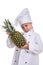 Puzzled serious chef girl in a cap cook. Girl holding pineapple. Human emotions, facial expression feeling