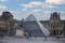 Pyramid of the Louvre museum in Paris with its buildings on the banks of the Seine river under a blue sky
