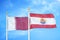 Qatar and French Polynesia two flags on flagpoles and blue cloudy sky