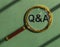 QnA acronym through magnifying glass on green background, top view. Concept of eco questions and answers. Q and A