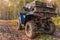 Quad bike on the road. A blue ATV POLARIS Quad bike stands on the road in the autumn forest. The SUV is covered in dirt close-up