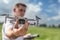 A quadcopter operator with a remote control out of focus holds a drone in front of him in focus outdoor