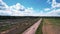 Quadcopter shooting of a passing white car on a sandy road past rows of graves in a large cemetery near a forest