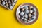 Quail eggs container and fresh eggs on yellow background. Top view