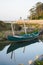 Quaint small boat next to shore in peaceful lagoon on bright day. Boat reflection on water.