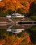 Quaint white house reflecting in a lake, surrounded by gorgeous fall foliage and autumn colors.