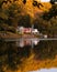 Quaint white house reflecting in a lake, surrounded by gorgeous fall foliage and autumn colors.