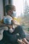 Quarantine, threat of coronavirus. Sad child and his teddy bear both in protective medical masks sits on windowsill and looks out