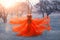 Queen in bright long elegant flying red dress poses for photo, woman with dark hair and crown on her head puts hands on