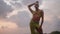 Queer black person poses in open dress, handmade jewelry stands on scenic sea cliff top above dramatic cloudy sky and