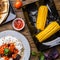 Quesadilla, salad with cottage cheese and tomatoes, two corn on wood table.