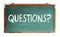 Questions? text word message in white chalk written on a wide green old grungy vintage wooden chalkboard or retro blackboard